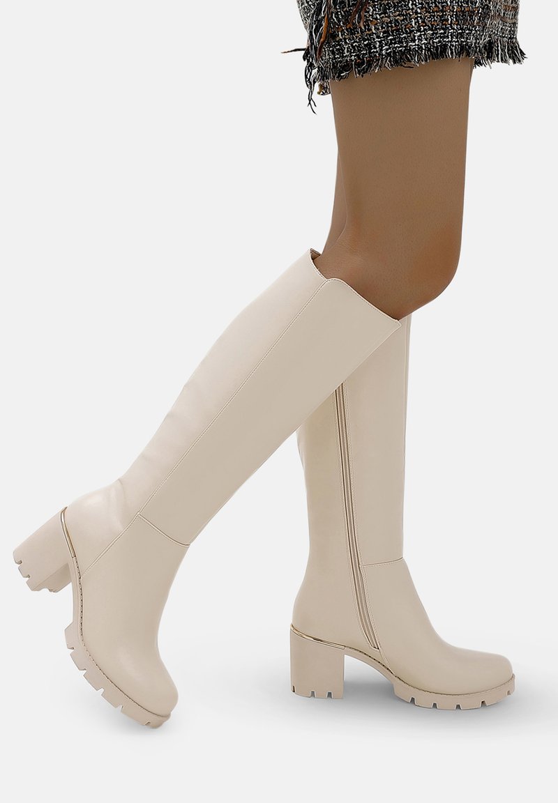 Botas beige hasta la rodilla, hechas de material sintético brillante, con un tacón grueso y suela texturizada, con un diseño sin costuras y costuras visibles.
