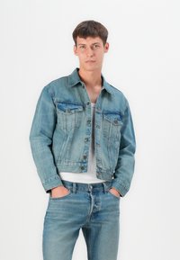 Light blue denim jacket with two chest pockets, button closure, and slightly faded texture, paired with matching light blue jeans.
