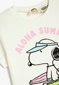 Hvid ribbet bomulds T-shirt med Snoopy grafik, en lys blå skygge, pink tekst der siger "ALOHA SUMMER" og farverige strandtilbehør.