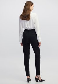 Schwarze, maßgeschneiderte Hose mit glatter Textur und elastischem Bund, kombiniert mit einer weißen Bluse mit langen Ärmeln. Slim-Fit-Design.