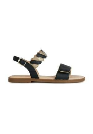 Sandalias de cuero negro con suela marrón, que presentan una tira ancha y detalles de tiras trenzadas, hebilla ajustable y diseño plano.