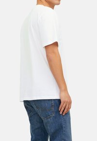 Weißes Baumwoll-T-Shirt mit kurzen Ärmeln, im entspannten Schnitt und geradem Saum, getragen mit blauen Denim-Jeans.