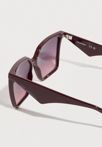 Bordó műanyag napszemüveg szögletes dizájnnal, átmenetes színű lencsékkel és ezüst "KARL LAGERFELD" logóval az oldalsó szárakon.