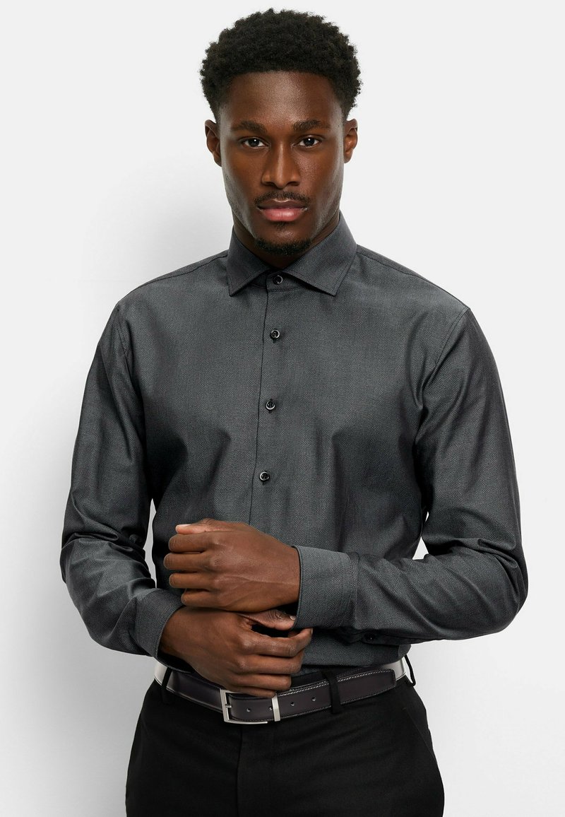 Dunkelgraues Hemd mit subtiler Textur und langen Ärmeln, ausgestattet mit schwarzen Knöpfen und einem klassischen Kragen, kombiniert mit einem dunklen Gürtel.