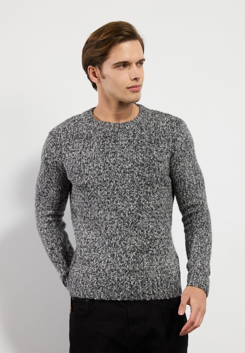 Gray knitted sweater with a textured pattern, ribbed cuffs and hem, round neck, fitted design. Worn over black pants.