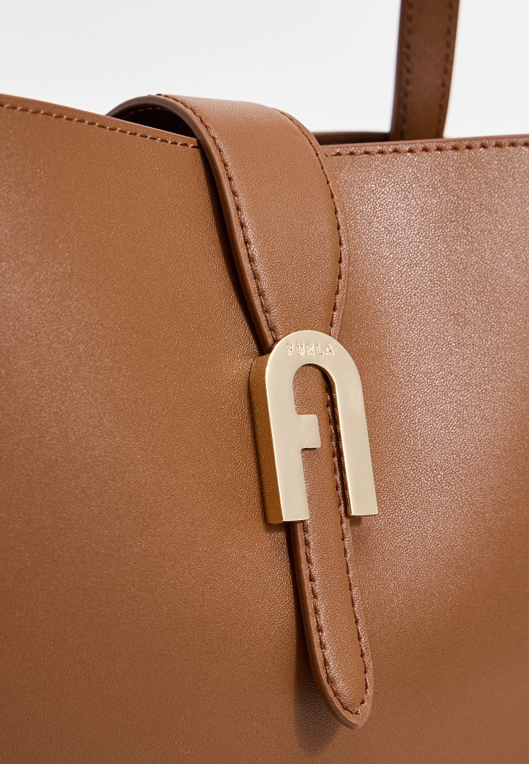 Brązowa skórzana torebka o gładkiej fakturze, wyróżniająca się wyraźnym złotym logo oraz eleganckim designem z górnym uchwytem.