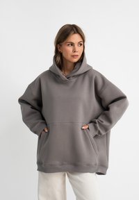 Felpa grigia oversize realizzata in materiale morbido, con cappuccio regolabile, grandi tasche frontali e polsini e orlo a costine.