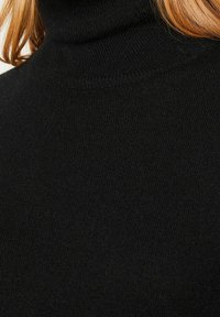 Pull à col roulé noir présentant une texture douce et des poignets côtelés. Vue en gros plan mettant en valeur la douceur du tissu et son design chaud.