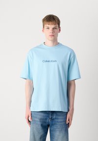 Lyseblå bomull t-skjorte med korte ermer, rund hals, og "Calvin Klein" logoen trykket i mørkeblått på forsiden.