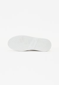 Semelle de basket blanche avec un motif circulaire texturé et le nom de la marque embossé sur la zone de la voûte plantaire, montrée sur un fond clair uni.