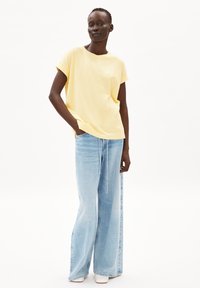 T-shirt giallo a maniche corte con scollatura rotonda, abbinato a jeans a gamba larga di colore blu chiaro con dettaglio a coulisse.
