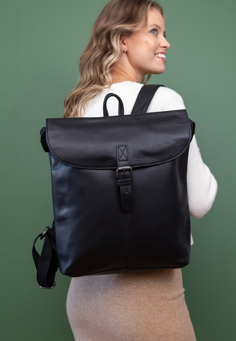 Sac à dos en cuir noir avec rabat pliable, fermeture à boucle métallique unique et bretelles réglables. Il dispose d'une poignée de transport en haut et d'une texture lisse.