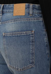 Leren denim jeans in lichtblauwe was, met een tan leren label op de achterkant van de taille met de tekst "BITE" en een achterzak met oranje stiksels.
