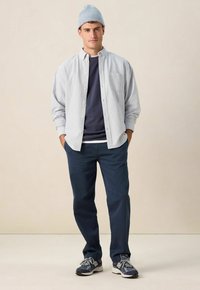 Lichtblauw-wit gestreept overhemd over een marineblauwe trui, gecombineerd met marineblauwe broek en grijze sneakers, afgewerkt met een lichtblauwe muts.