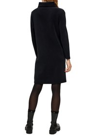 Czarna sukienka z polaru z wysokim kołnierzem, długimi rękawami i prostym krojem, zestawiona z czarnymi teksturowanymi botkami za kostkę.