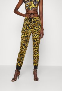 Svarta träningsoveraller med ett guldigt virvlande barockmönster, elastisk midja och muddarna. Matcher med en matchande kort topp.