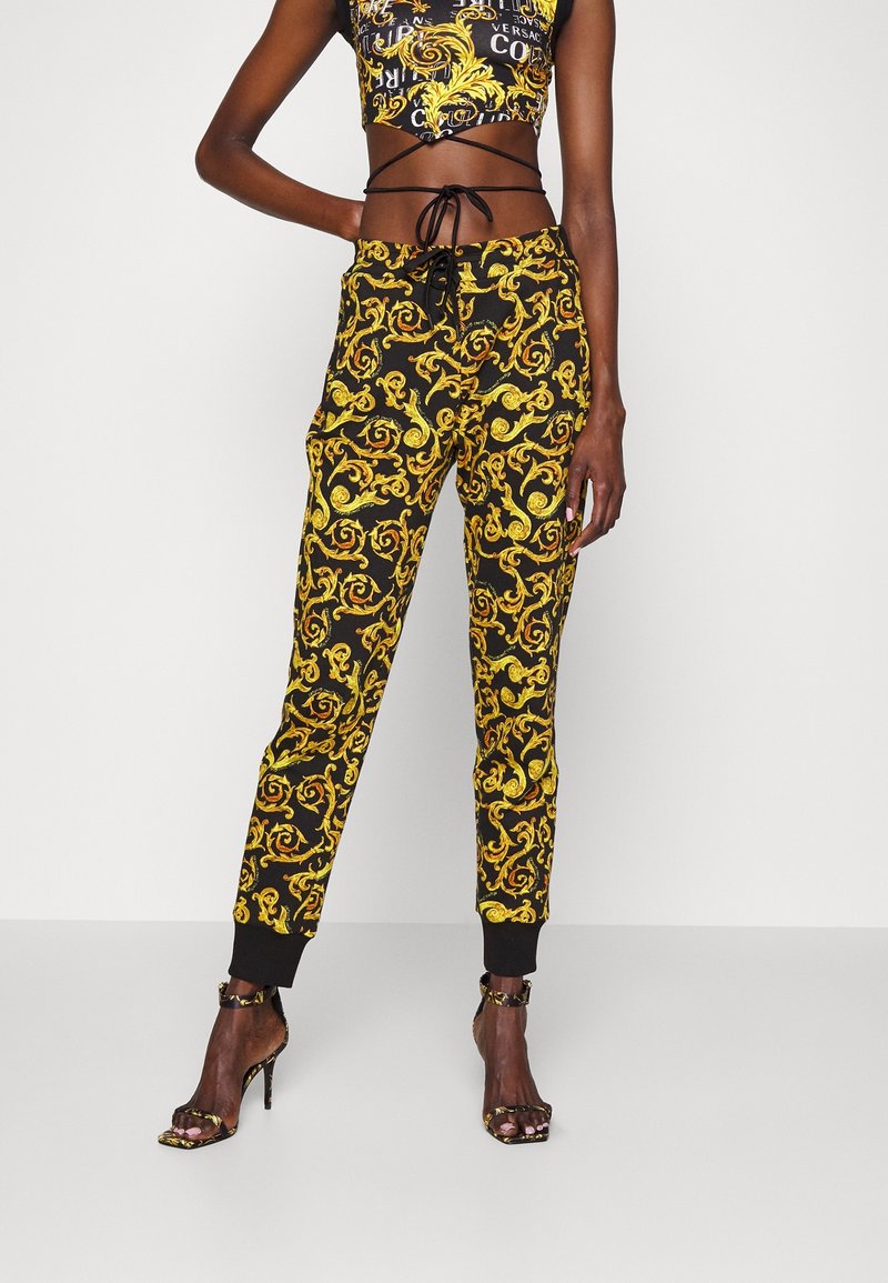 Svarta träningsoveraller med ett guldigt virvlande barockmönster, elastisk midja och muddarna. Matcher med en matchande kort topp.