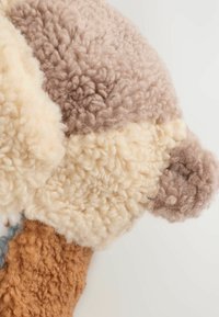 Textured fabric pillow featuring beige, light brown, and rust colors. Soft, fluffy wool-like material with a patchwork design and rounded edges.