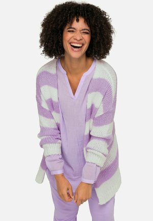 Lichtpaars gestreepte gebreide cardigan met brede mouwen over een bijpassende lichtpaarse top. Model lacht en toont een ontspannen, losse pasvorm.
