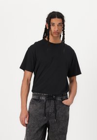 Black short-sleeve t-shirt with a crew neckline and subtle logo detail. Paired with gray elastic waist pants featuring a drawstring and pocket.