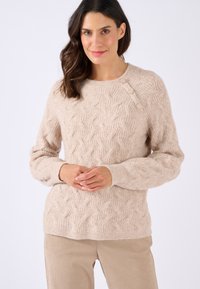 Pull en maille beige avec col rond et accent de trois boutons à l'épaule. Manches longues légèrement bouffantes. Mélange de laine doux et texturé.