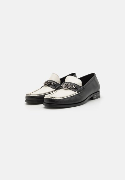Black and white leather loafers with a silver chain accent and stitching details, featuring a low heel and rounded toe design.