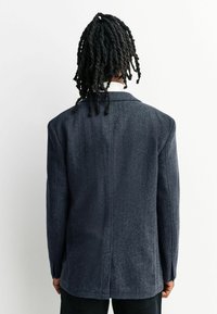 Dunkelblaues Blazer aus texturiertem Stoff mit Fischgrätenmuster. Verfügt über strukturierte Schultern, einen einzelnen Rückenschlitz und knöpfbare Manschetten.