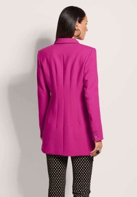 Fuchsia blazer met een getailleerde pasvorm, met een gekartelde kraag, achterste plooien en knoopmanchetten, gecombineerd met zwart-wit gestreepte broeken.