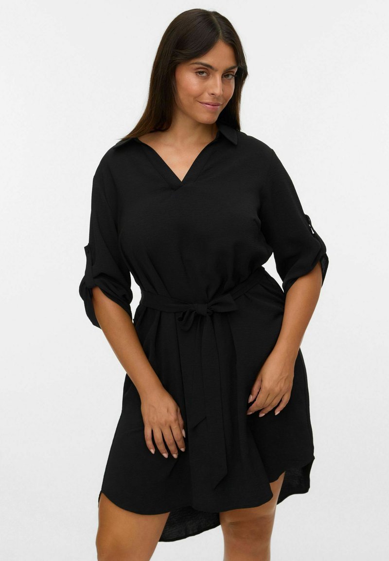 Zwarte jurk met een V-hals, korte opgerolde mouwen en een strikceintuur in de taille. Gemaakt van zachte stof met een relaxte silhouet en zijsplitten.