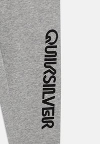 Grå sweatpants i mjukt material, med en vertikal svart logotryck på vänster ben. Avslappnad design med en bekväm passform.