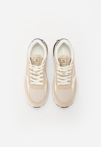 Beige og hvite sneakers med mesh- og semsket skinn-paneler, rund tå, frontsnøring og svart såle. Har et logo-merke på tungen.