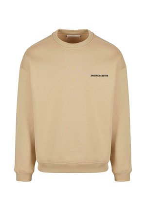 Bež kootud, millel on ümar kaelus, ribidega varrukad ja põhi. Ees on must tekst "ANOTHER COTTON".