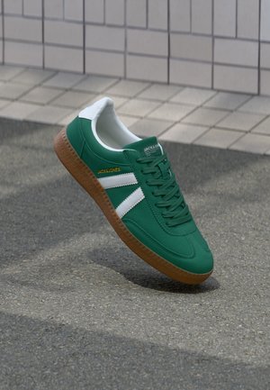 Grüne Sneakers mit weißen Streifen, einer strukturierten braunen Gummisohle und einem glatten Stoffoberteil, das Schnürsenkel und ein Logodetail an der Seite aufweist.