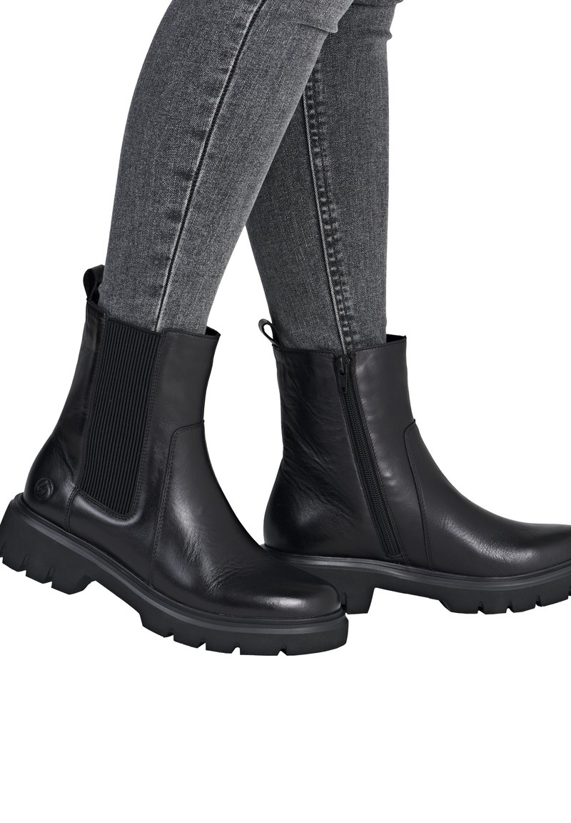 Black leather ankle boots with elastic side panel, side zipper, and rugged sole. Smooth finish with textured accents. Gray skinny jeans visible.