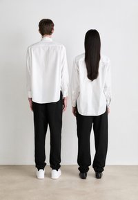 Baltos ilgos rankovės marškiniai, dėvimi su juodomis kelnėmis. Vienas asmuo avintis baltus sportinius batelius, o kitas - juodus batus. Minimalistinis dizainas, neutralios spalvos.