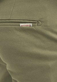 Pantaloni in cotone verde oliva con una texture liscia, dotati di una tasca posteriore etichettata "JACK & JONES" con dettagli bianchi e blu.