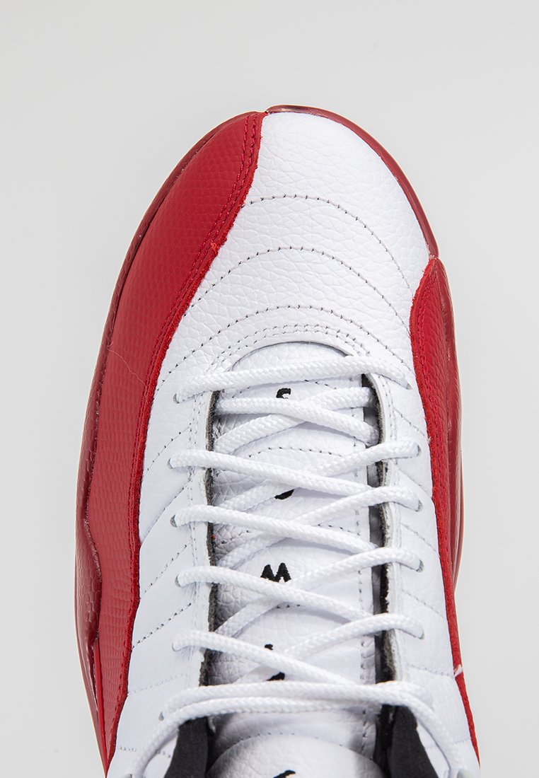 Białe i czerwone skórzane buty sportowe o teksturowanym wykończeniu, z przeszywanym wzorem, białymi sznurowadłami i czarnymi akcentami.