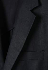 Mörkblå blazer tillverkad av texturerad tyg, med spettslag och en enda bröstficka med subtila sömnadsdetaljer.