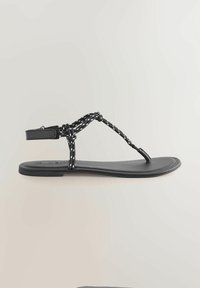 Sandalia plana negra con una tira de tela con acentos blancos, un separador de dedos y una delgada correa en el tobillo. Diseño simple con una suela lisa.