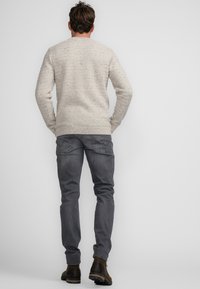 Light beige knitted sweater with a textured pattern, paired with dark gray jeans. Brown ankle boots complete the outfit from a rear view.
