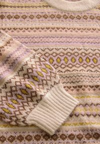 Pull en tricot avec une texture douce, des couleurs pastel légères et des motifs géométriques en rose, marron et jaune, avec des poignets et un col côtelés.