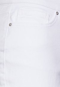 Jeans de mezclilla blancos con un bolsillo trasero con un pequeño remache metálico, textura suave y sutiles detalles de costura.