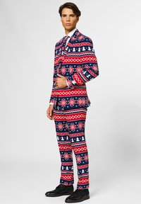 Marineblauer Anzug mit einem rot-weißen Feiertagsmuster, das Schneeflocken, Bäume und geometrische Formen zeigt. Abgerundet mit schwarzen Schuhen.