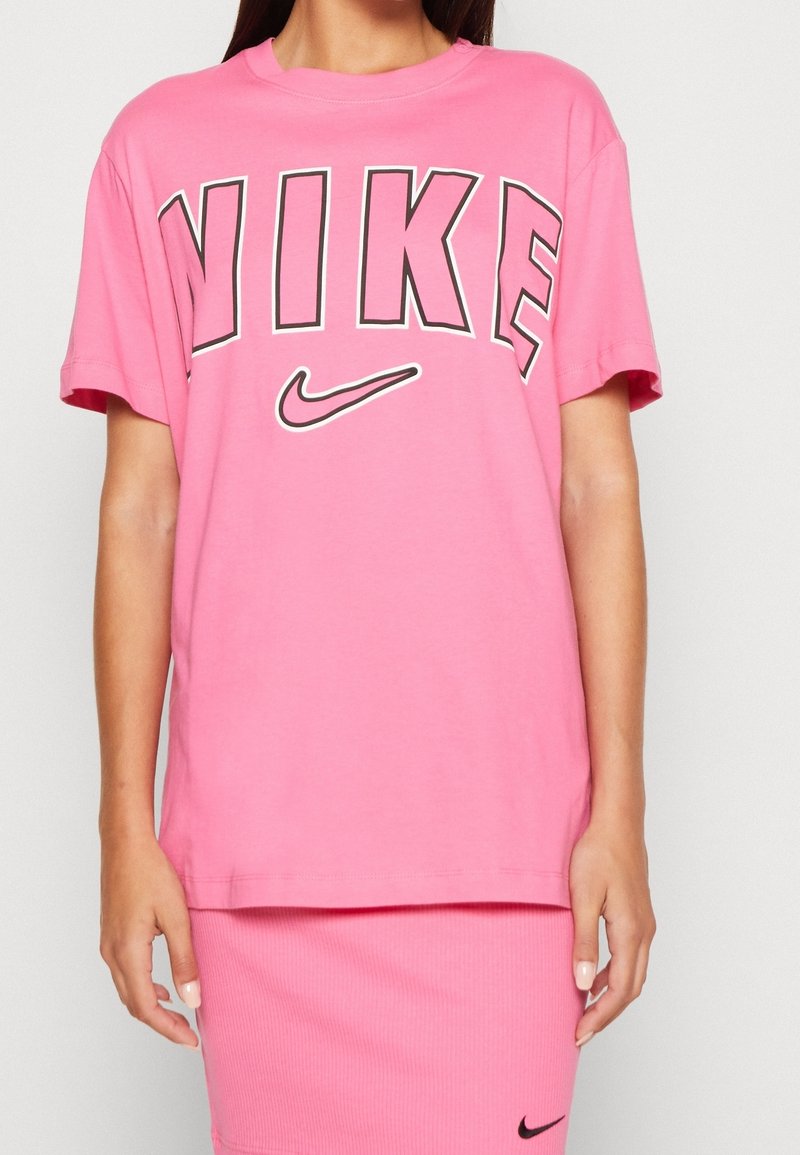 Rosa bomullströja med svart "NIKE" grafik och logotyp. Avslappnad passform, korta ärmar, rund halsringning. Slät textur, minimalistisk design.