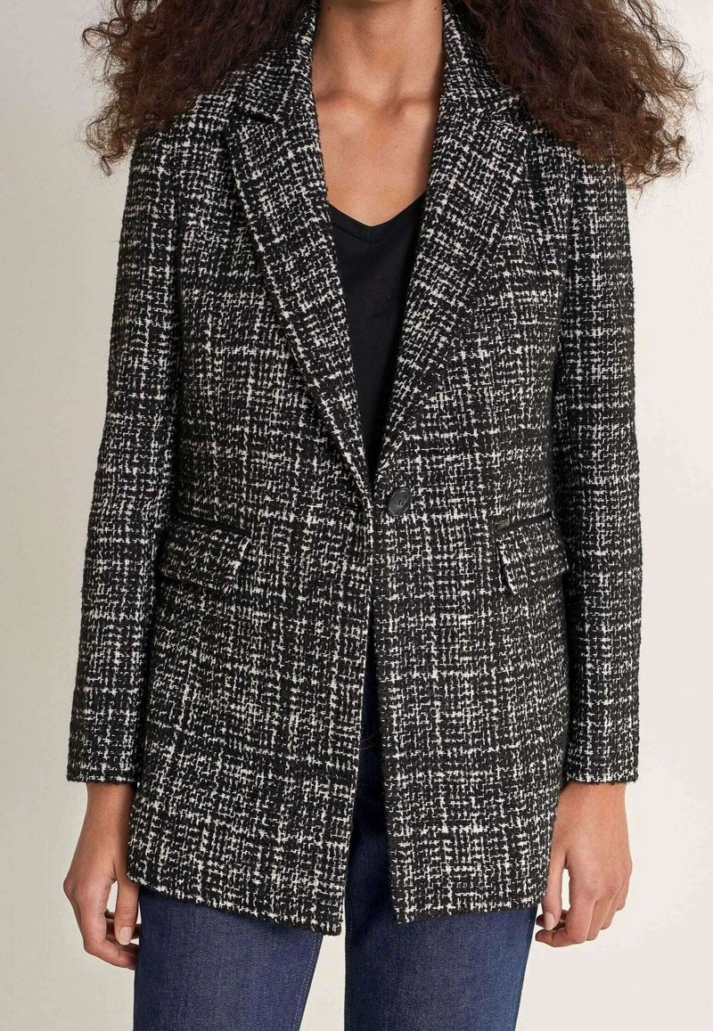 Veste à motif noir et blanc avec un tissage texturé, col à revers, deux poches avant et une fermeture à un bouton.