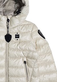 Giacca puffy beige chiaro con una texture lucida, cappuccio, tasca con zip e toppe nere del marchio sulle spalle. Presenta un cappuccio con cordini.