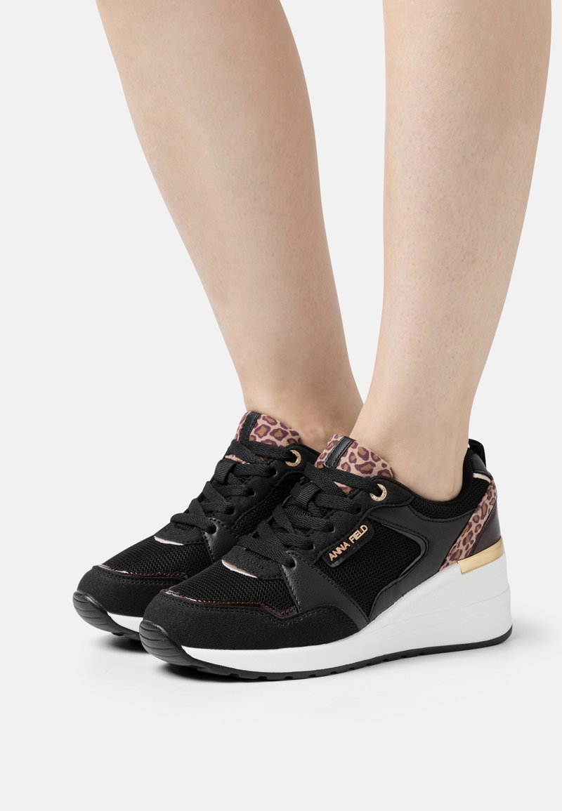 Black sneaker with a mesh and suede upper, leopard print accents on the heel, gold hardware, and a white wedge sole.