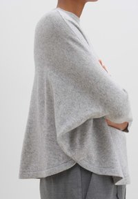 Světle šedý svetr vyrobený z měkké pleteniny, s uvolněným střihem, spadenými rameny a zakřiveným lemem pro volnou siluetu.