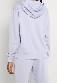 Ljust lila huvtröja med dragsko, mjukt material, ribbade muddar och nederkant. Har en slät textur och avslappnad passform.