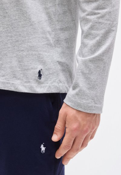 Camisa cinzenta de manga comprida com um logótipo azul-marinho, combinada com calças azul-marinho com um pequeno logótipo branco. Tecido macio com textura suave.